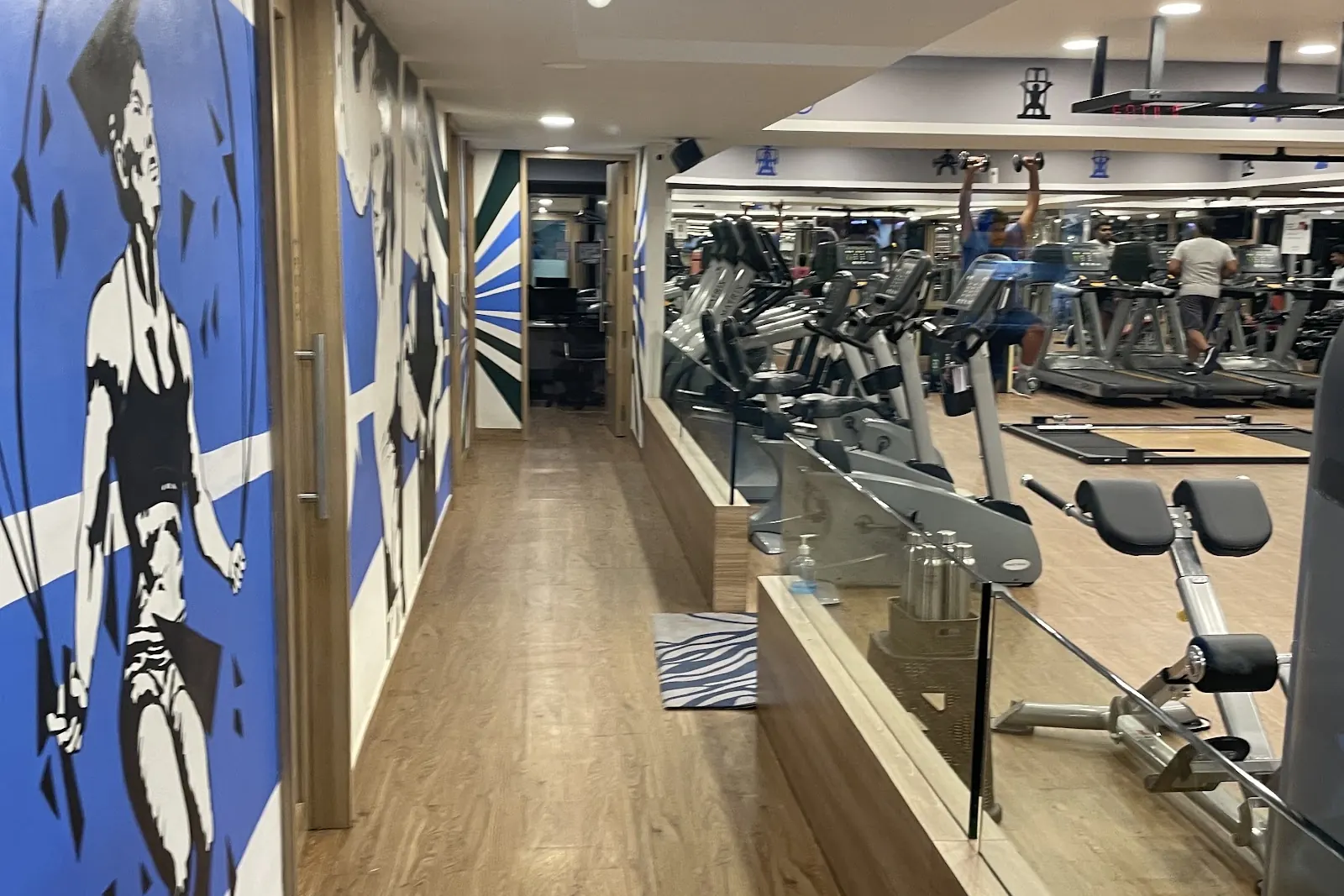 Corridor with a blue and white mural of an athlete, a mirrored cardio floor on the right