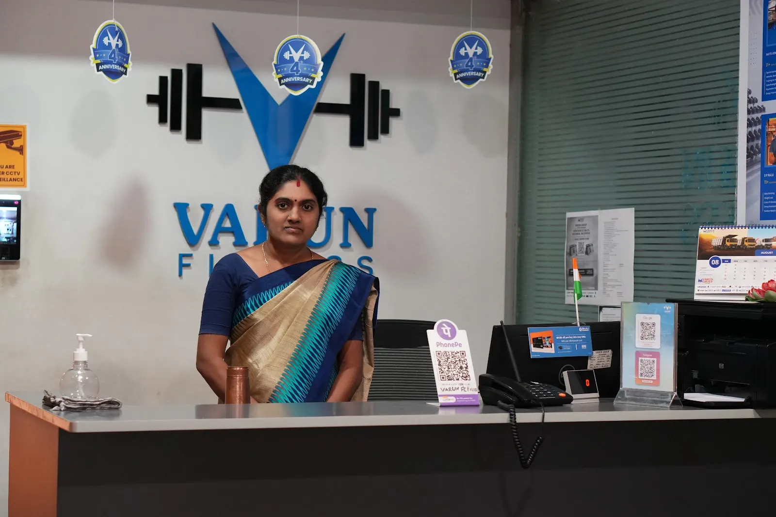 A woman in a saree stands at the reception desk under the Varun Fitness logo